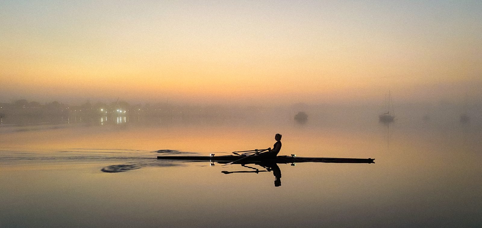 A lone sculler gliding through morning mist