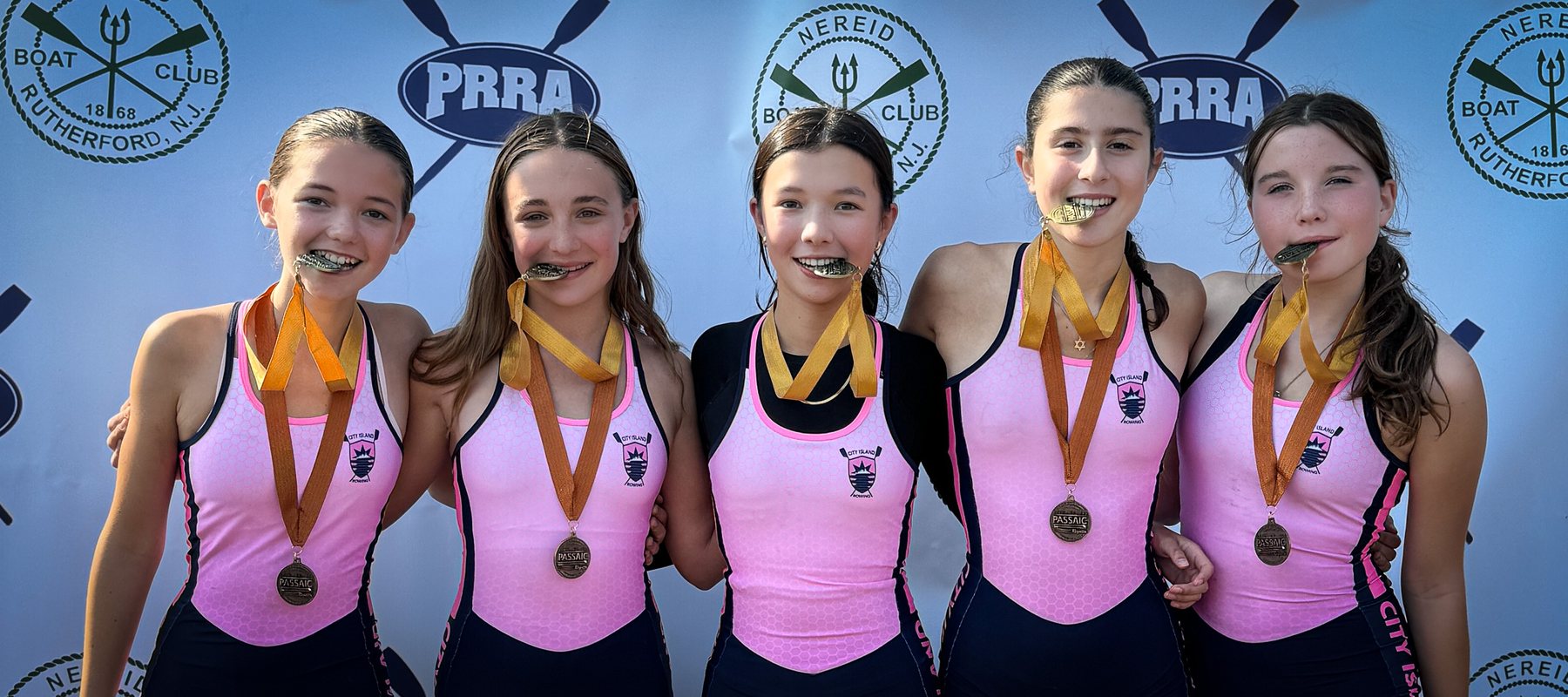 Five novice rowers in pink, medals in their teeth