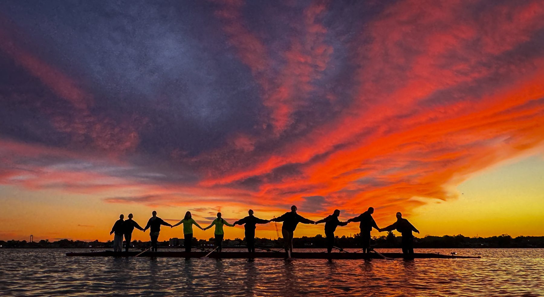 Girls standing on the boats, linked hands raised, against a blazing sunset